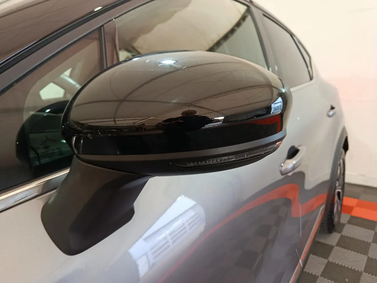 Rétroviseur noir brillant côté gauche en gros plan sur Renault Captur gris foncé 2024, avec poignée de porte visible.