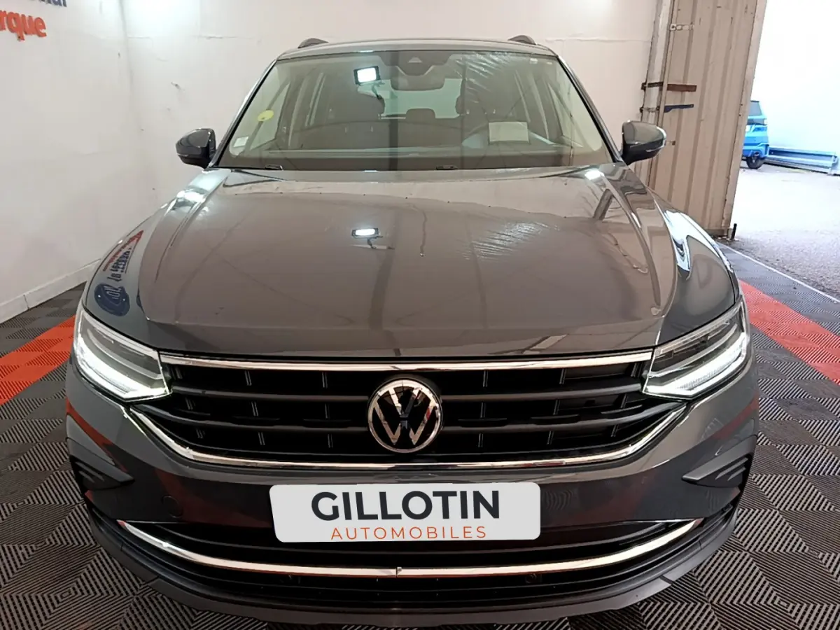 Vue frontale d'un Volkswagen Tiguan gris clair avec calandre chromée et phares LED allumés en intérieur showroom.