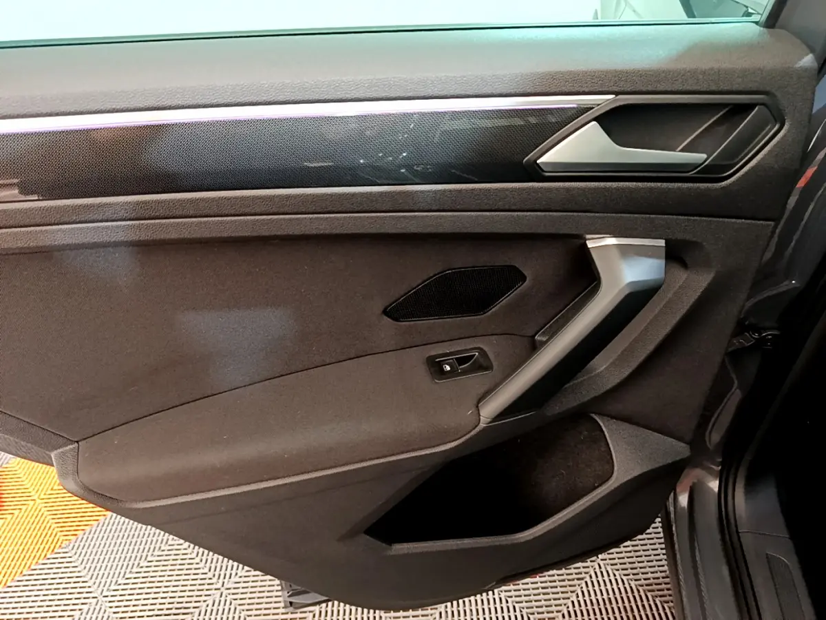 Vue rapprochée de la porte côté gauche du Volkswagen Tiguan 2021, garniture noire avec poignée argentée et haut-parleur intégré.