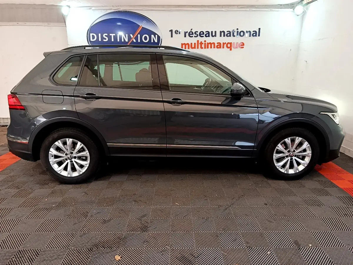 Profil côté droit d'un Volkswagen Tiguan gris clair 2021 garé en intérieur avec jantes alliage et rétroviseurs noirs.