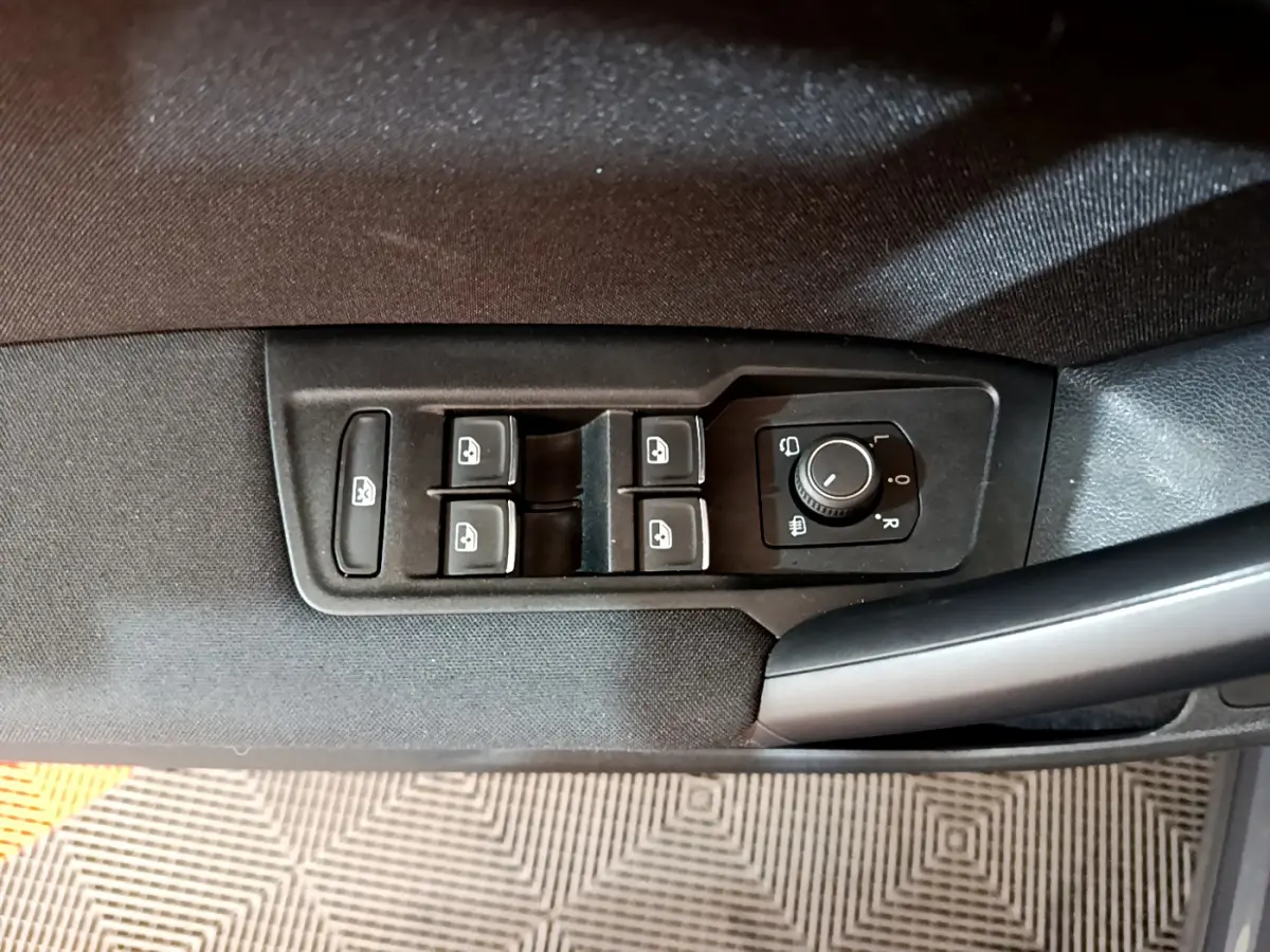 Gros plan sur les commandes de lève-vitres et réglage des rétroviseurs côté conducteur du Volkswagen Tiguan gris clair 2021.