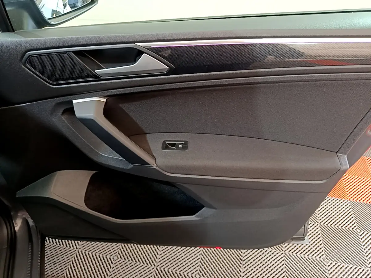 Vue rapprochée de la porte côté gauche intérieure du Volkswagen Tiguan gris clair, avec poignée argentée et garniture noire.