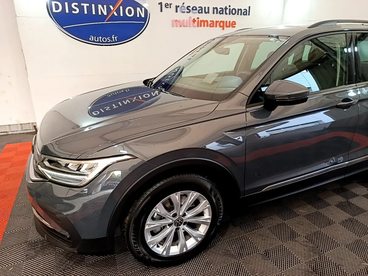 Vue 3/4 avant droit d'un Volkswagen Tiguan gris clair avec jantes alliage et phares LED dans un showroom.