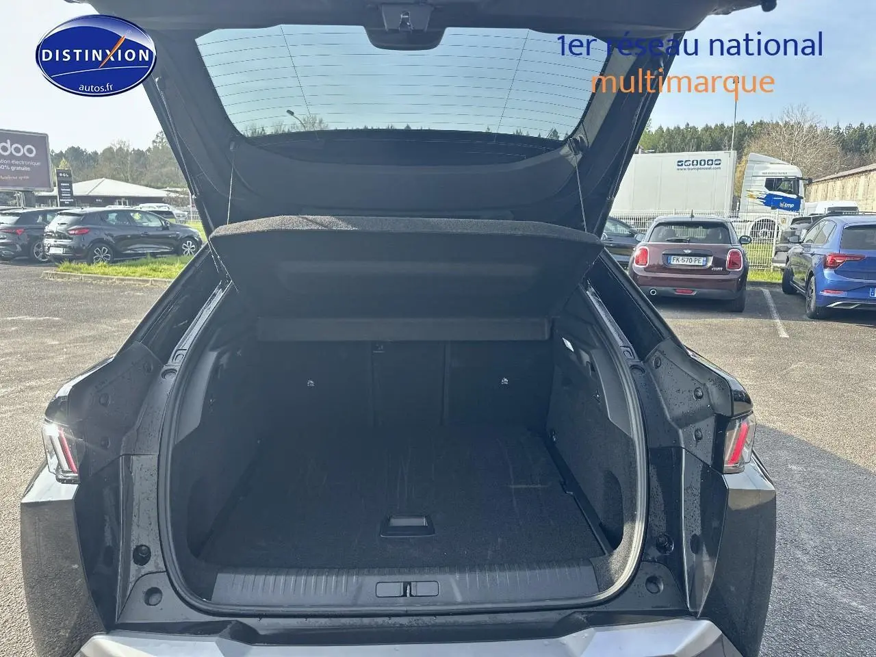 Coffre ouvert d’un Peugeot 3008 noir perla nera, vue arrière en extérieur sur parking ensoleillé.