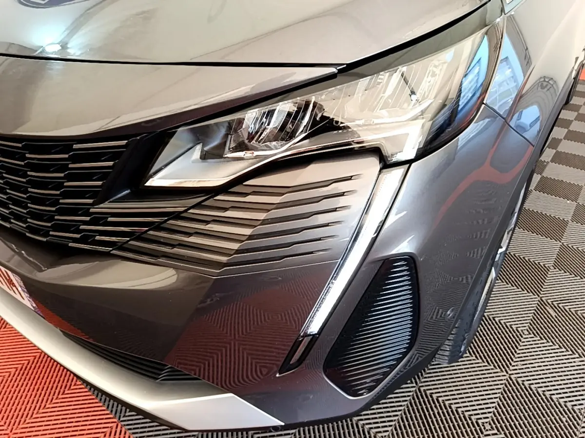 Gros plan sur l'avant droit gris foncé du Peugeot 3008 2022, mettant en valeur le phare et la calandre distinctive.
