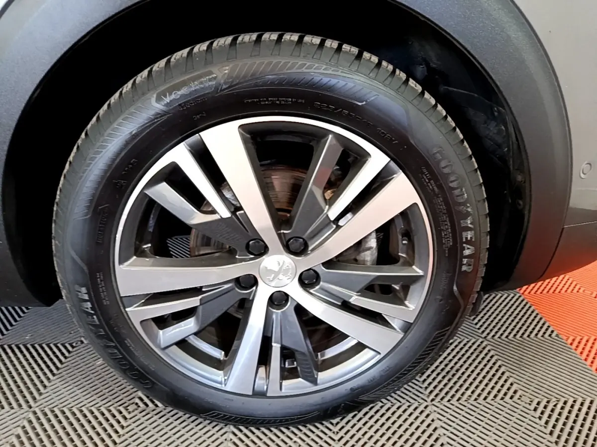 Gros plan sur la roue avant droite d’un Peugeot 3008 gris foncé, jante alliage à cinq branches doubles.
