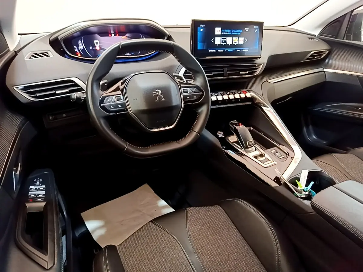 Vue intérieure du poste de conduite du Peugeot 3008 gris foncé, avec volant compact, écran tactile central et tableau de bord digital.