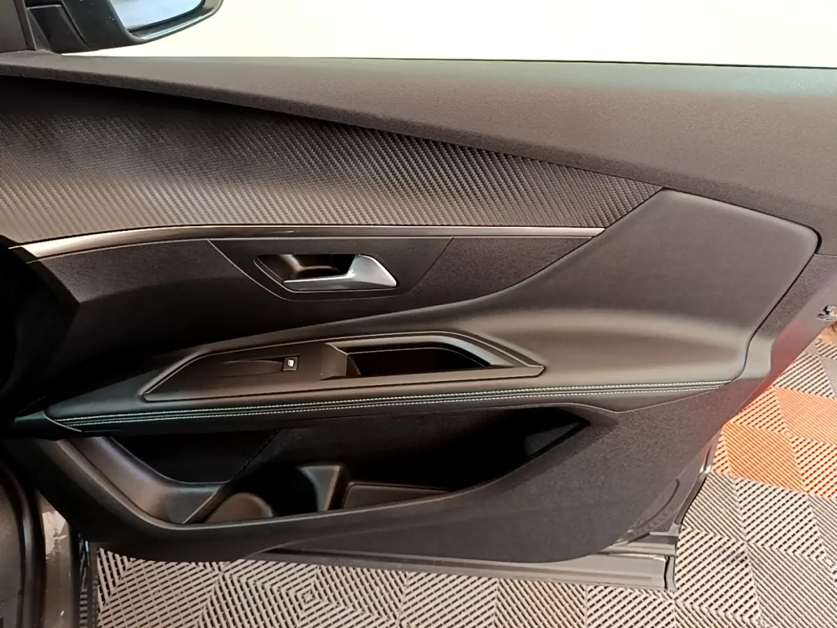 Intérieur côté gauche de la porte avant d’un Peugeot 3008 gris foncé, avec garniture noire et surpiqûres blanches.