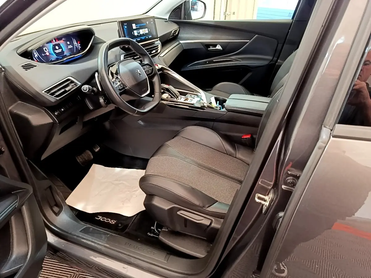 Vue intérieure côté conducteur du Peugeot 3008 gris foncé, avec tableau de bord digital et sièges en tissu et cuir.