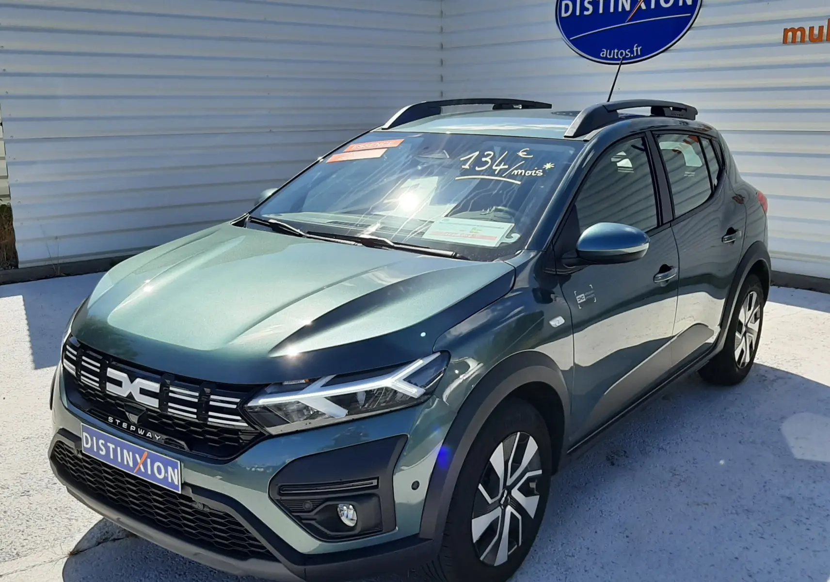 Vue 3/4 avant droite d'une Dacia Sandero Stepway 2025 vert cèdre avec barres de toit et calandre noire distinctive.