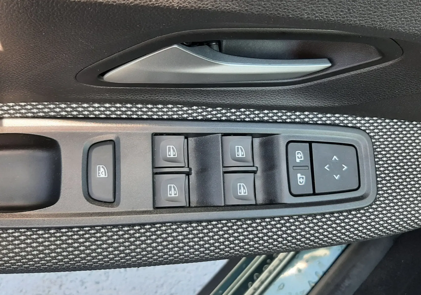 Gros plan sur la commande des vitres et la poignée intérieure côté gauche d’une Dacia Sandero Stepway vert cèdre.