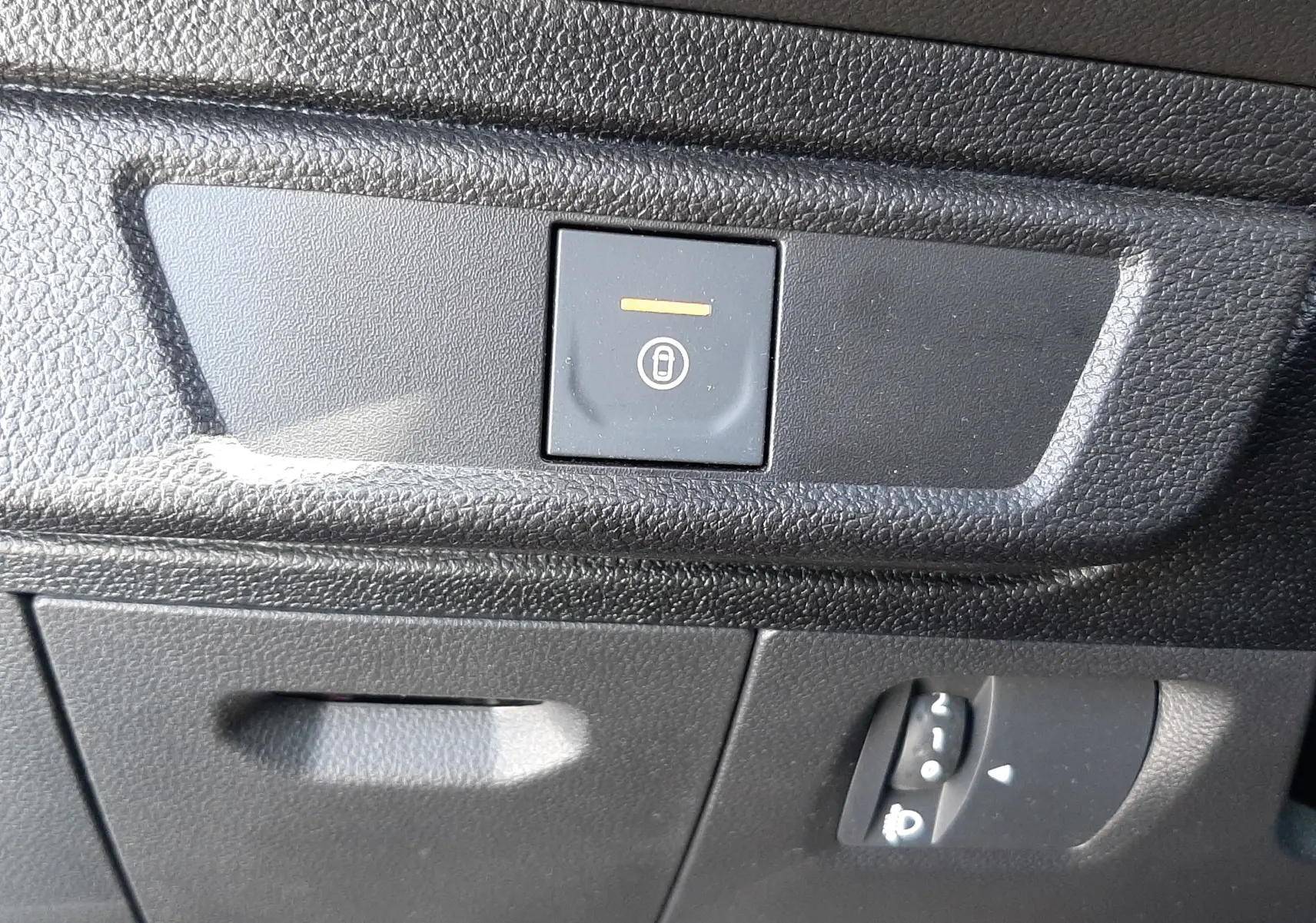 Gros plan sur le bouton de verrouillage centralisé et le réglage des phares sur la console inférieure noire du Dacia Sandero Stepway.