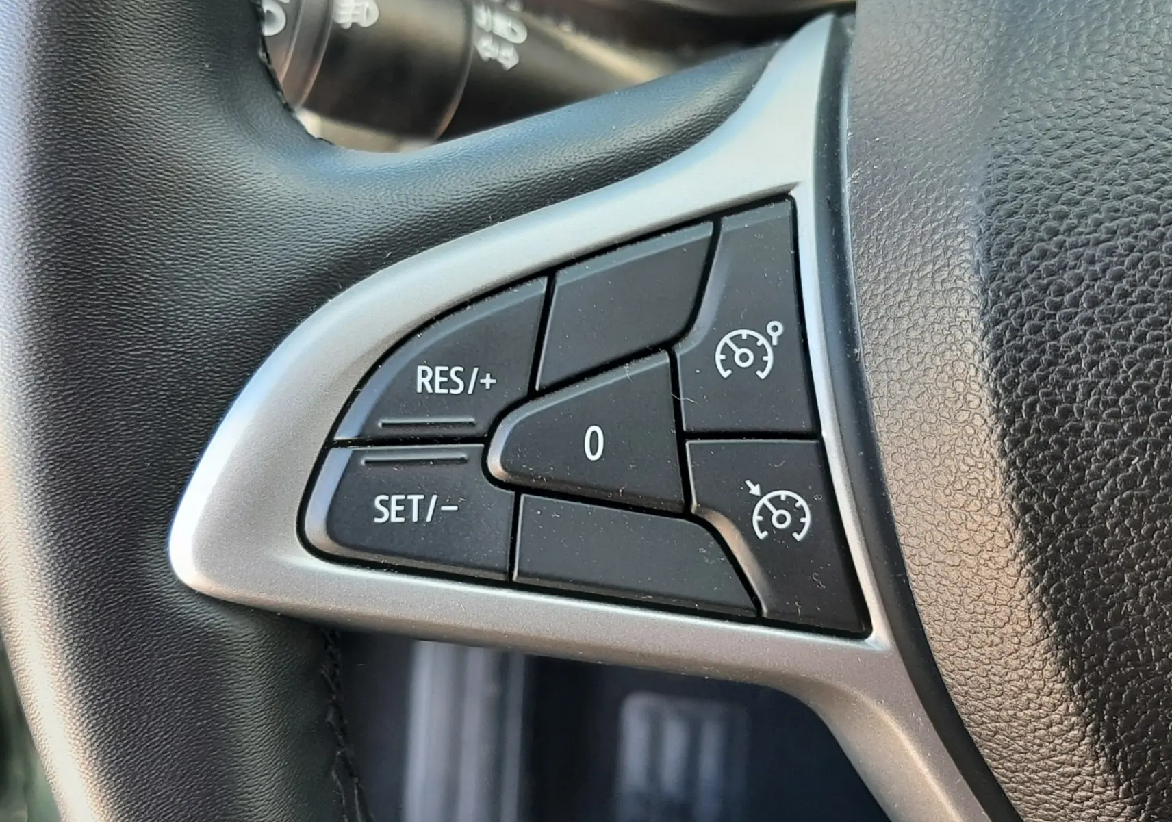 Gros plan sur les commandes de régulateur de vitesse au volant noir du Dacia Sandero Stepway 2025, intérieur gris.