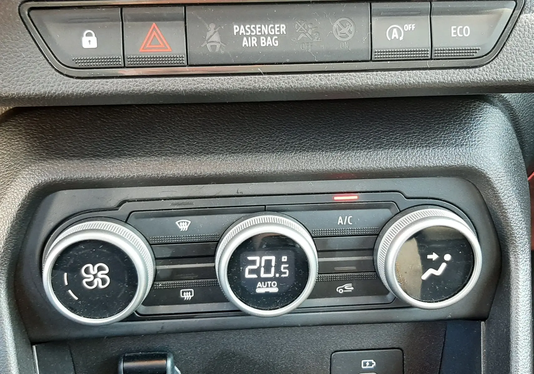 Gros plan sur la console centrale noire de la Dacia Sandero Stepway avec commandes de climatisation et boutons de sécurité.