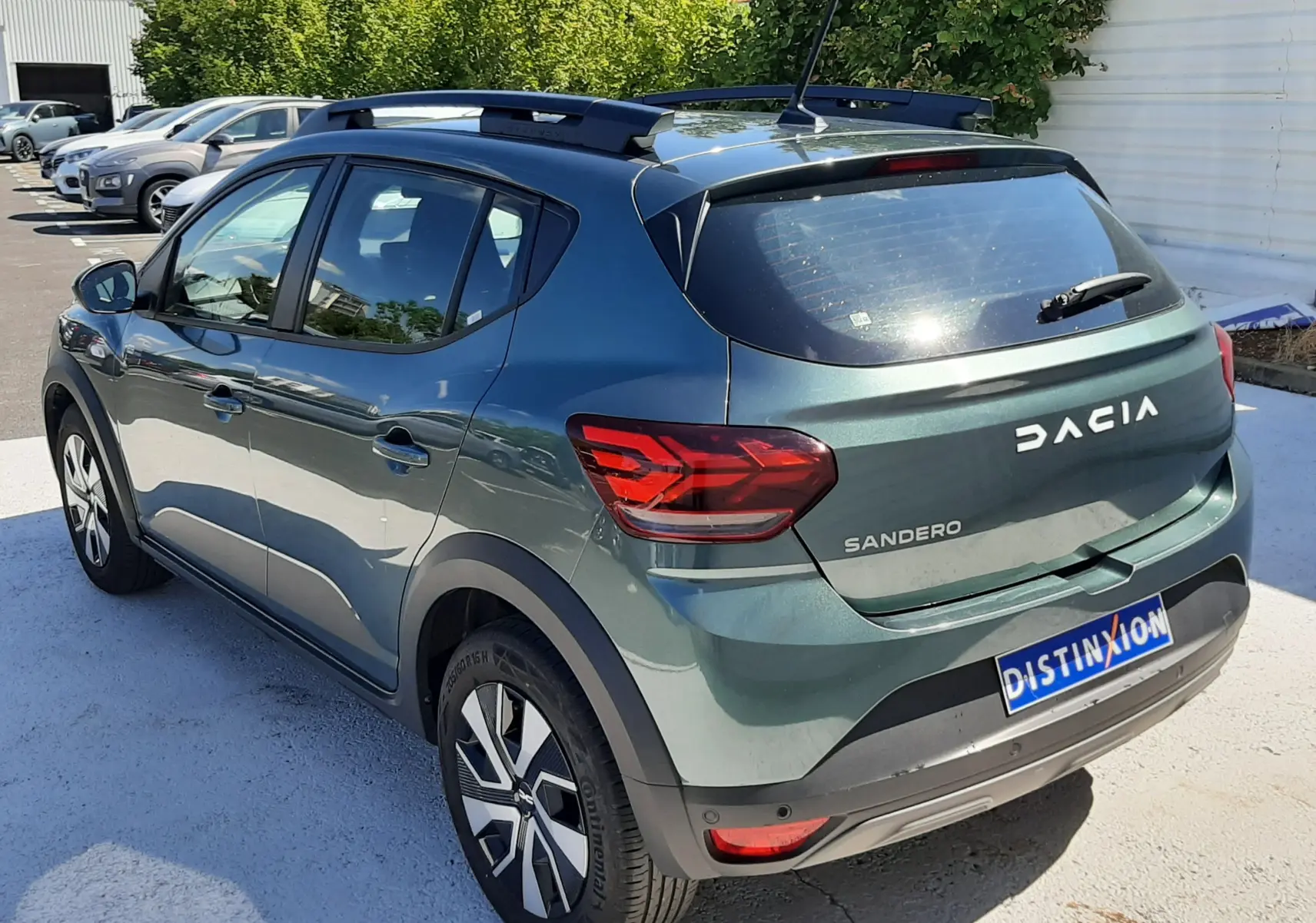 Vue 3/4 arrière droite d'une Dacia Sandero Stepway 2025 vert cèdre avec barres de toit et feux arrière LED.