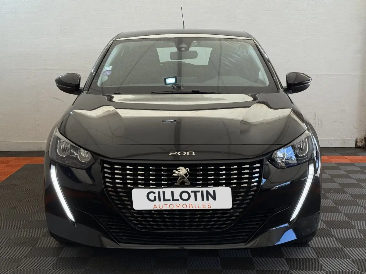 Vue frontale d'une Peugeot 208 noire avec calandre distinctive et feux LED en forme de griffes allumés