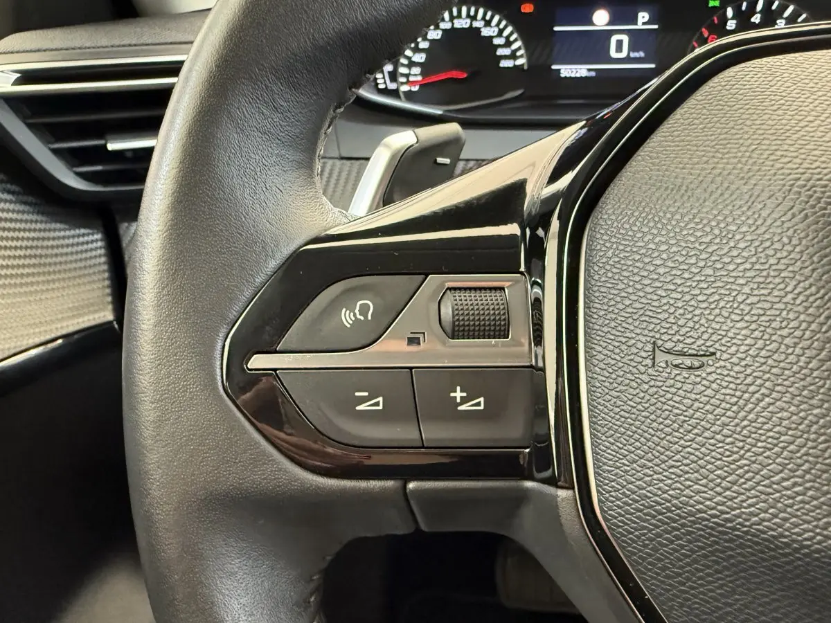 Gros plan sur le côté gauche du volant cuir noir de la Peugeot 208 2021, avec commandes vocales et volume.