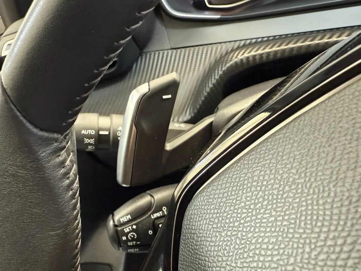 Gros plan sur la commande au volant noir de la Peugeot 208 PureTech 100, soulignant les boutons multifonctions.