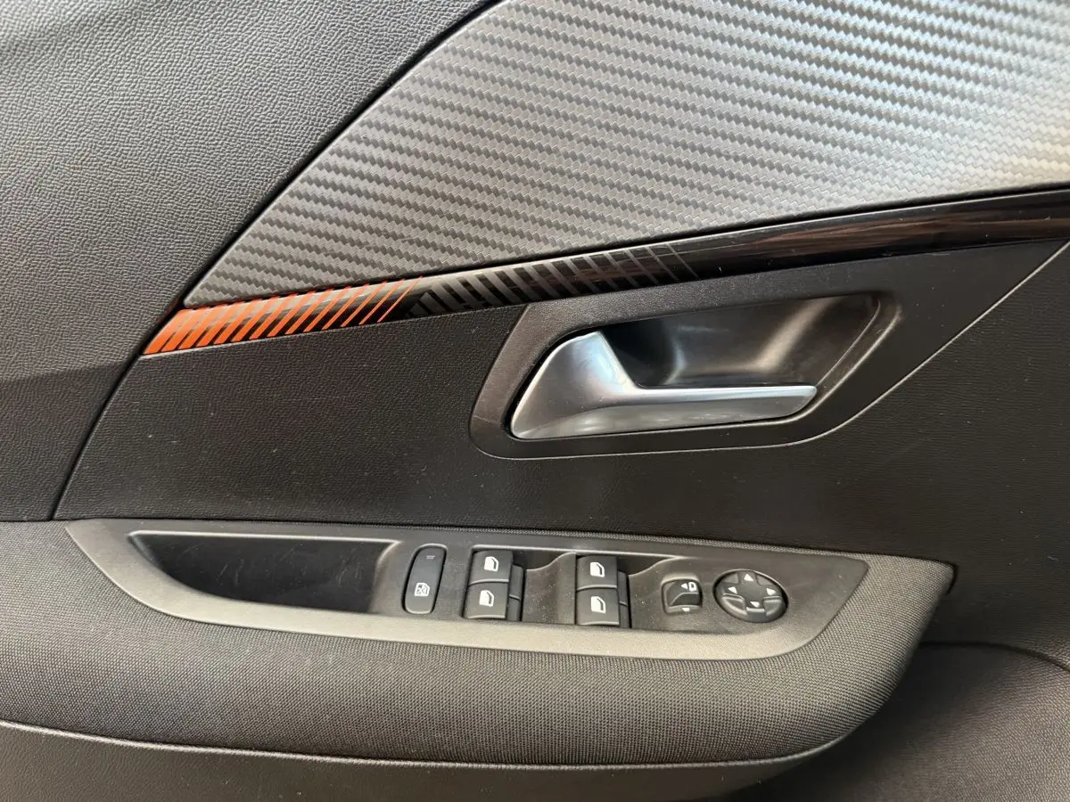 Poignée intérieure côté gauche de la Peugeot 208 noire, avec commandes des vitres et décor carbone orange.