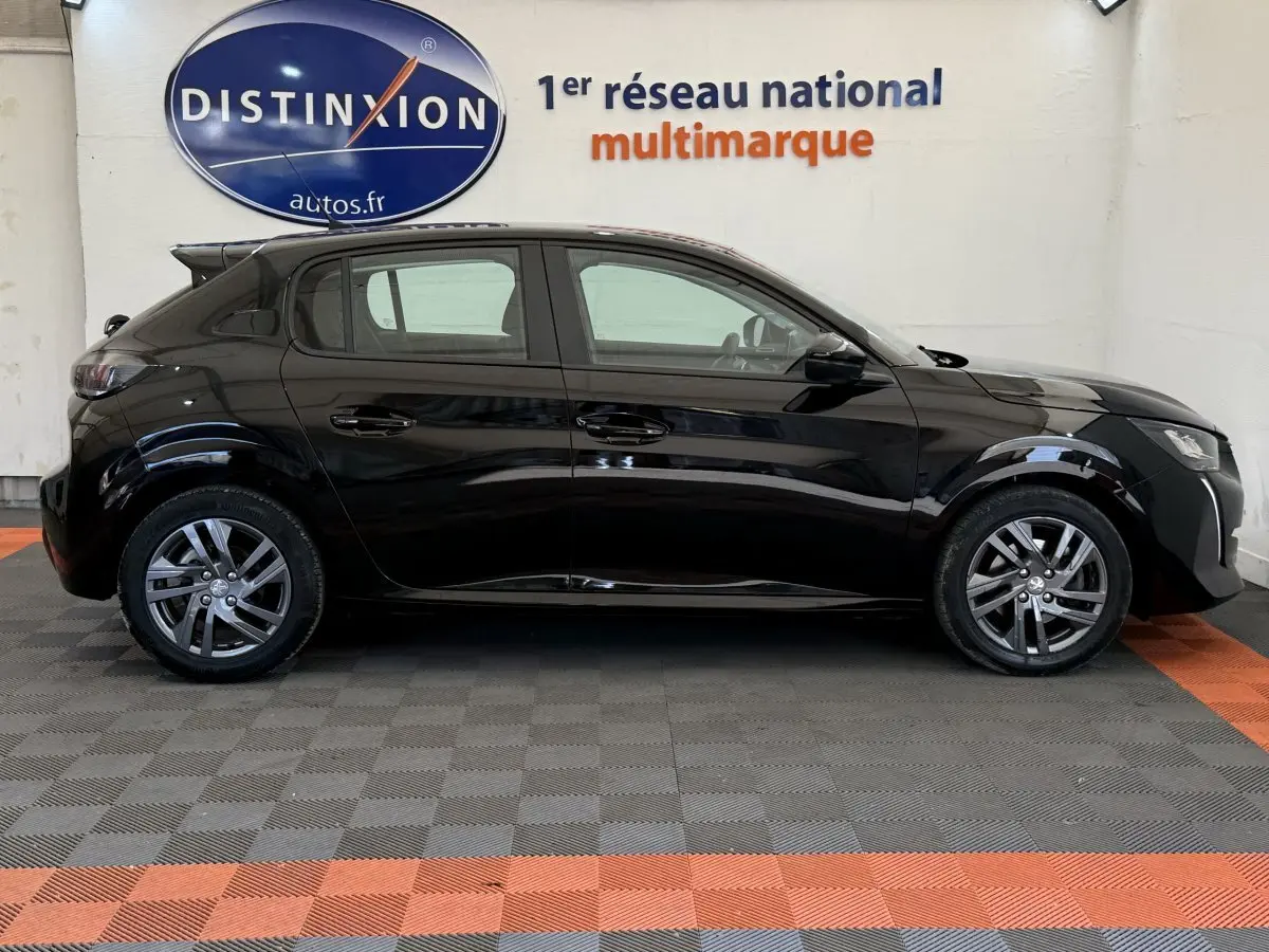 Peugeot 208 noire vue de profil côté gauche, stationnée en intérieur avec jantes alliage et vitres teintées.