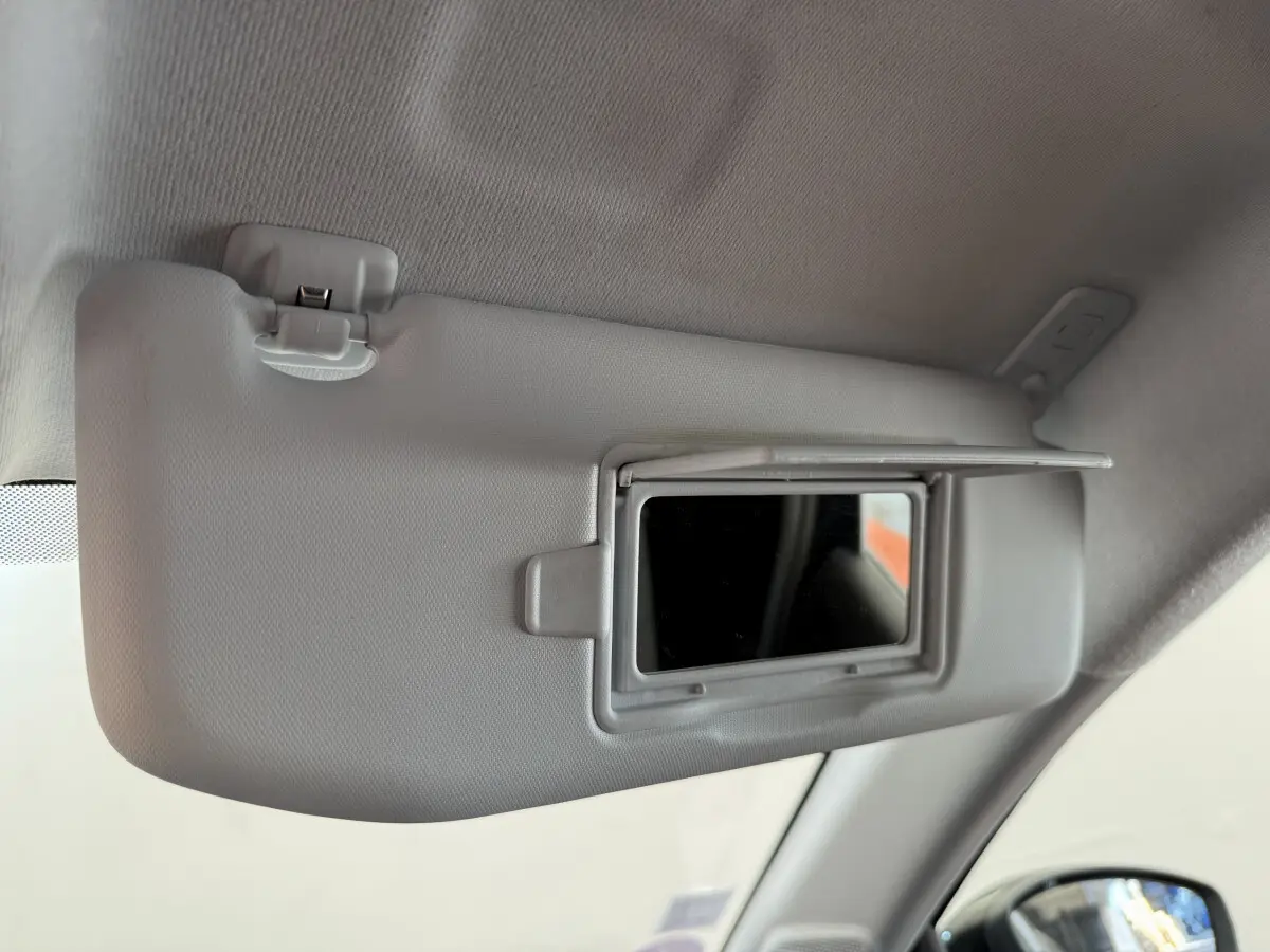 Miroir de courtoisie ouvert sur le pare-soleil côté conducteur d'une Peugeot 208 noire, vue intérieure rapprochée.