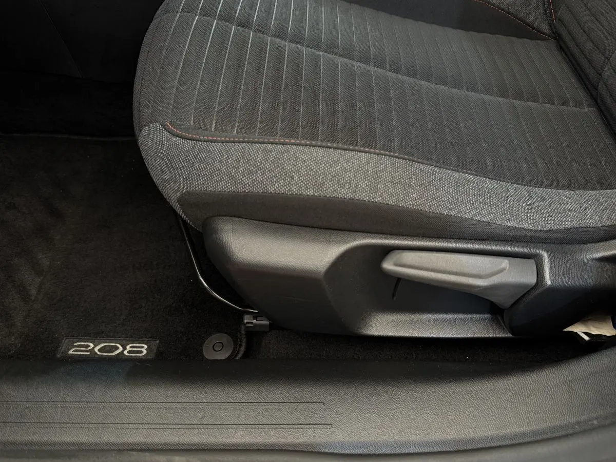 Gros plan sur le siège avant tissu gris et noir de la Peugeot 208 avec logo 208 sur le tapis de sol noir.
