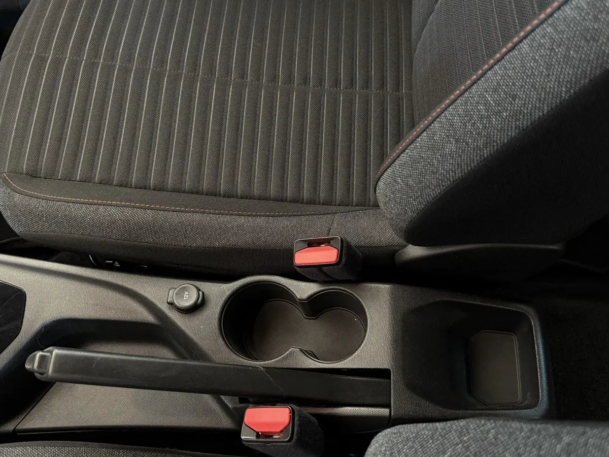 Vue rapprochée de la console centrale noire avec frein à main et sièges tissu gris foncé à surpiqûres rouges Peugeot 208.