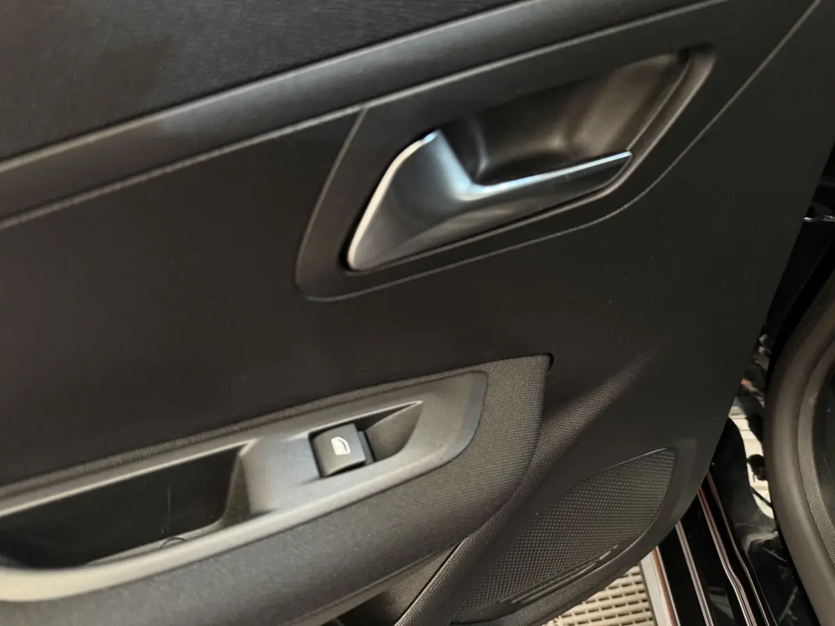 Gros plan sur la porte avant gauche noire du Peugeot 208 2021, montrant la poignée et le bouton de lève-vitre.