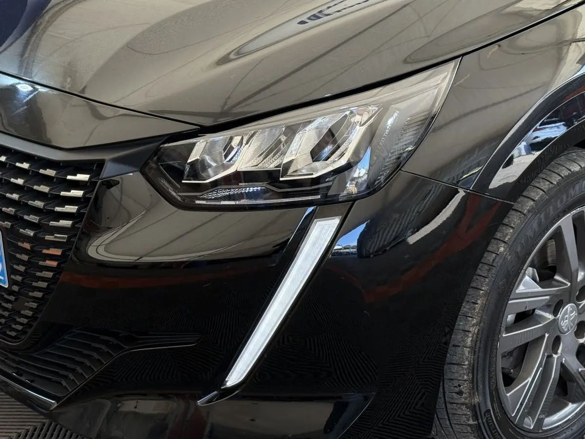 Gros plan sur l'avant droit noir de la Peugeot 208 2021, mettant en valeur le phare LED et la calandre distinctive.
