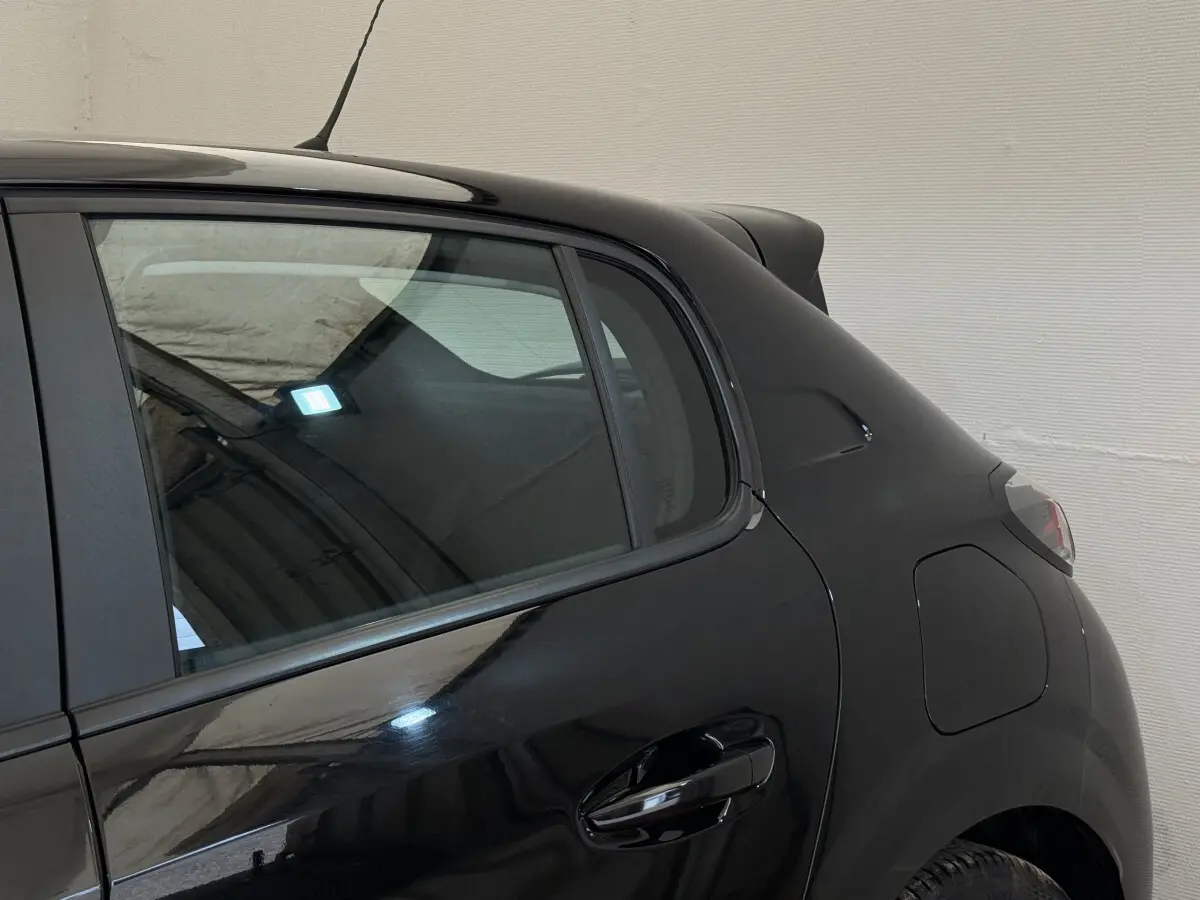 Vue côté arrière droit de la Peugeot 208 PureTech 100 noire, mettant en valeur la porte arrière et l'aile arrière.