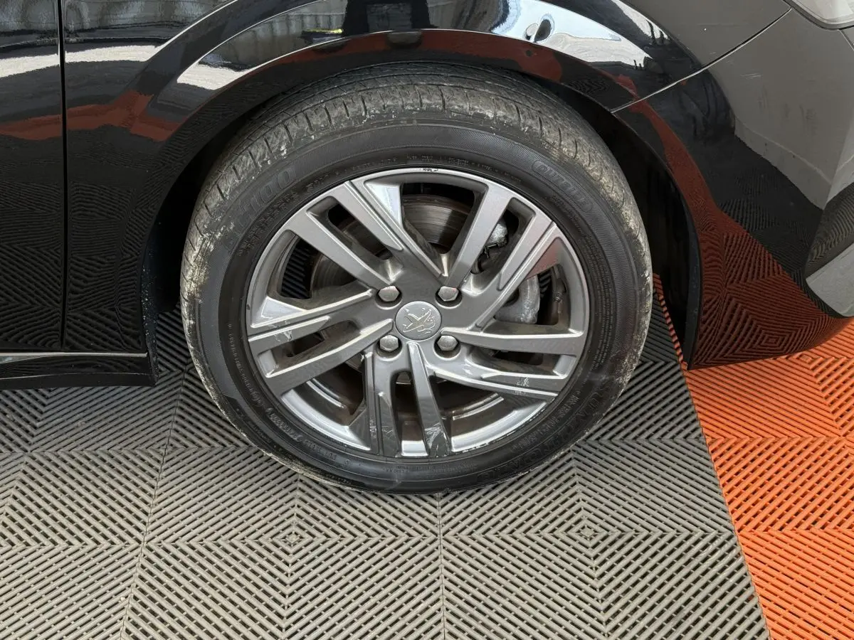 Gros plan sur la roue avant droite noire d'une Peugeot 208 2021, jante alliage gris argenté avec logo lion central.