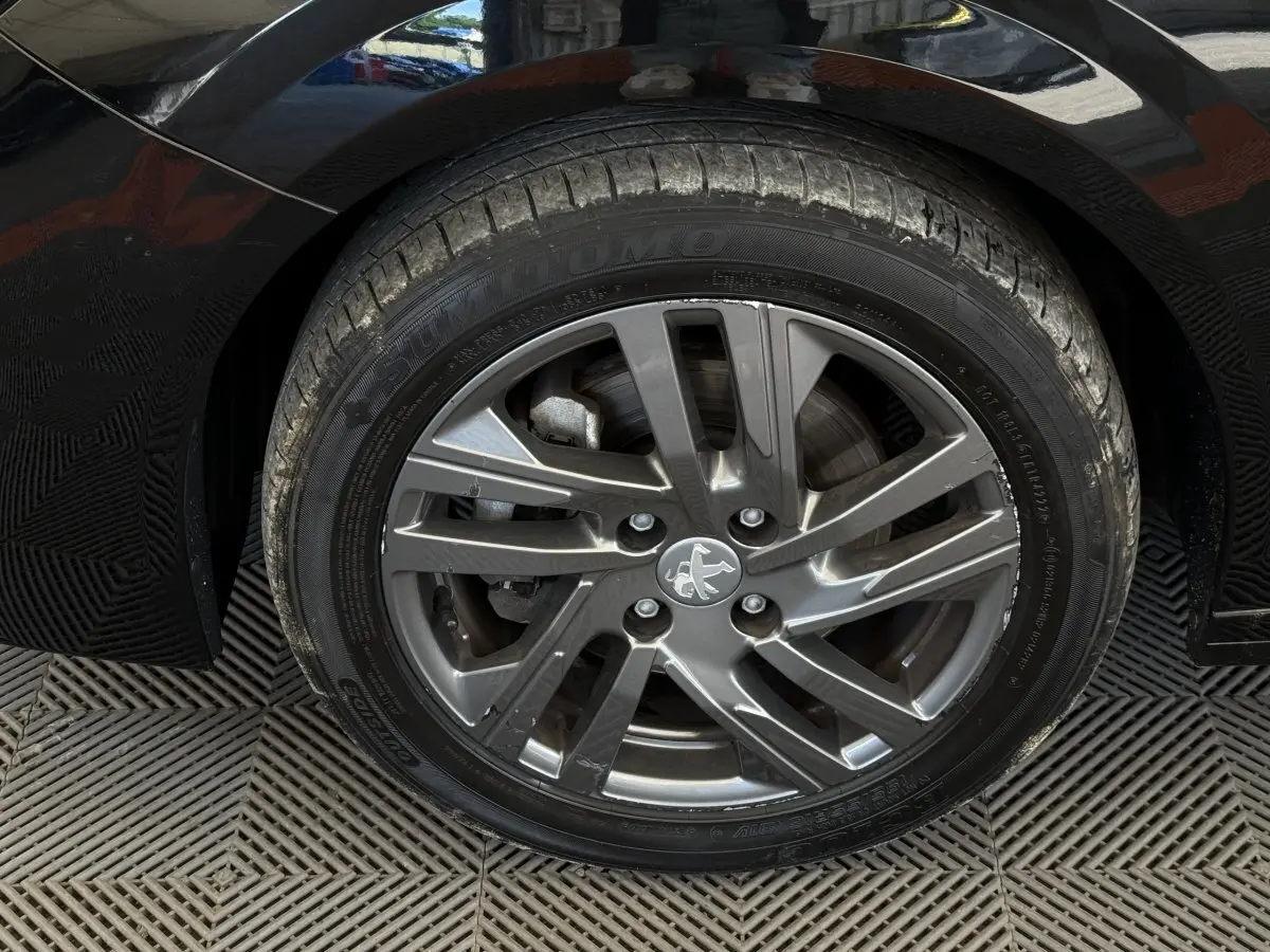 Gros plan sur la roue avant droite noire d'une Peugeot 208 2021 avec jante alliage gris foncé et logo lion central.