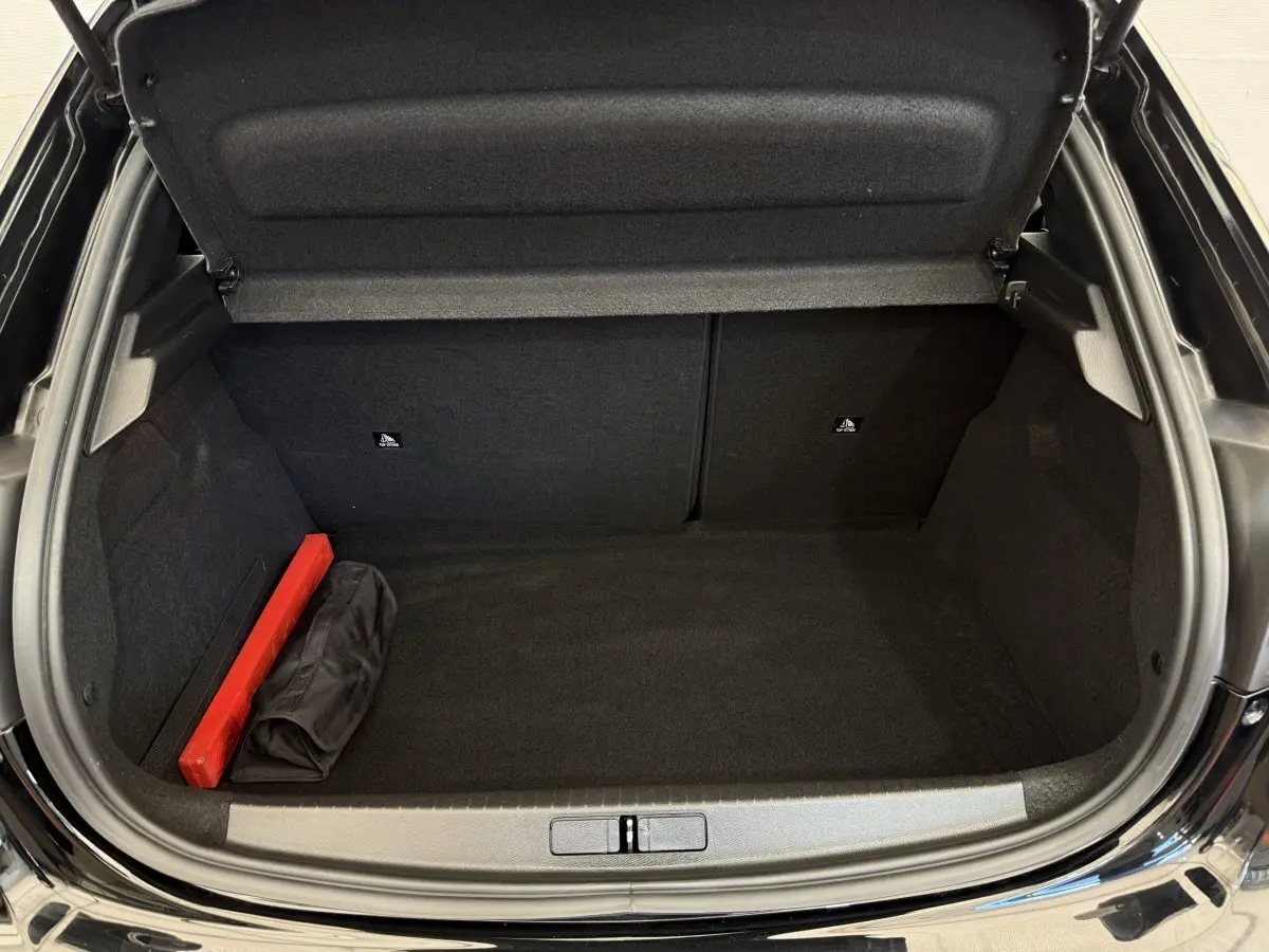 Coffre ouvert noir de la Peugeot 208 PureTech 100, montrant un espace vide avec un triangle de signalisation rouge.
