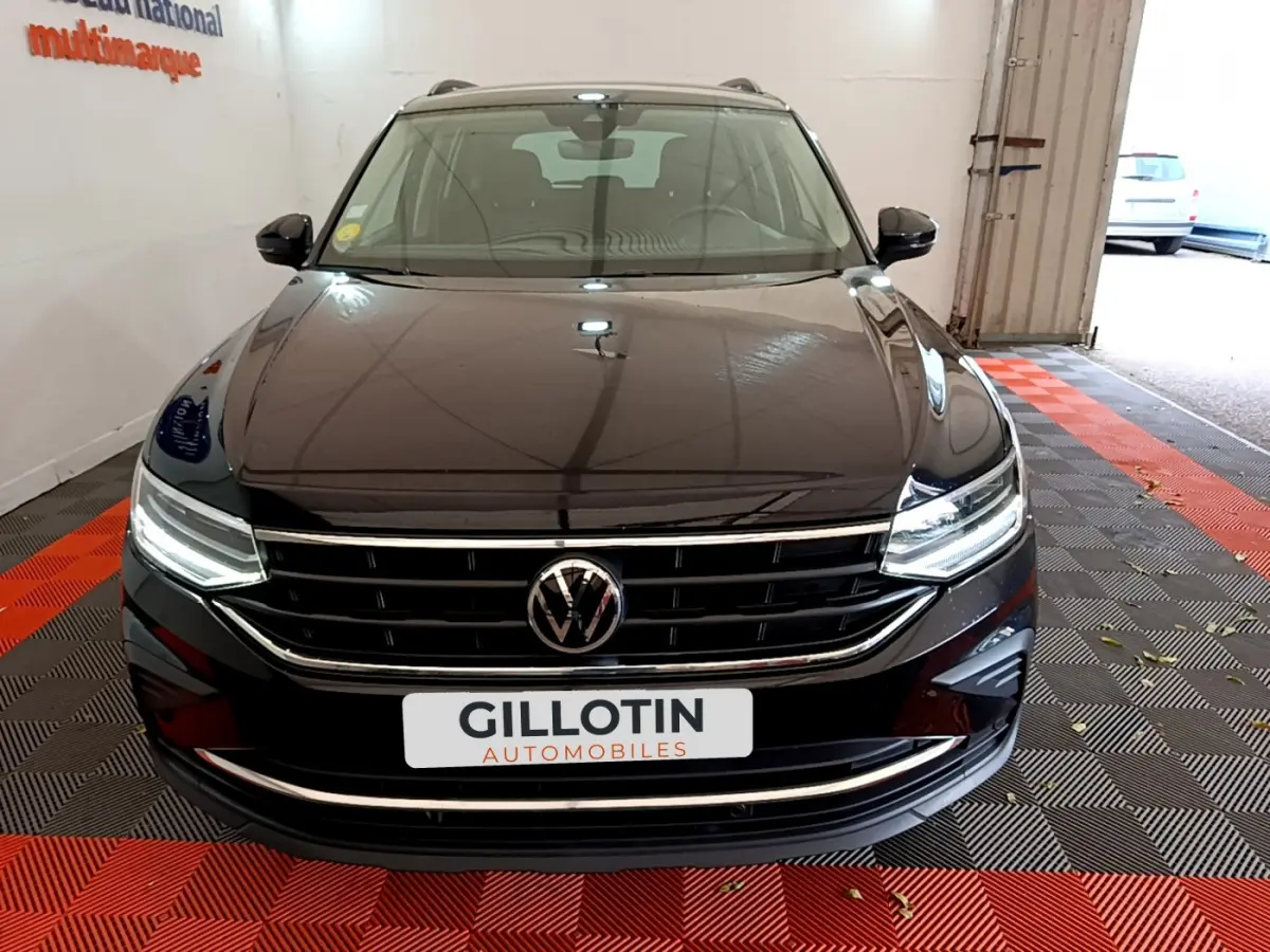 Vue frontale d'un Volkswagen Tiguan noir avec calandre chromée et phares LED allumés dans un garage.