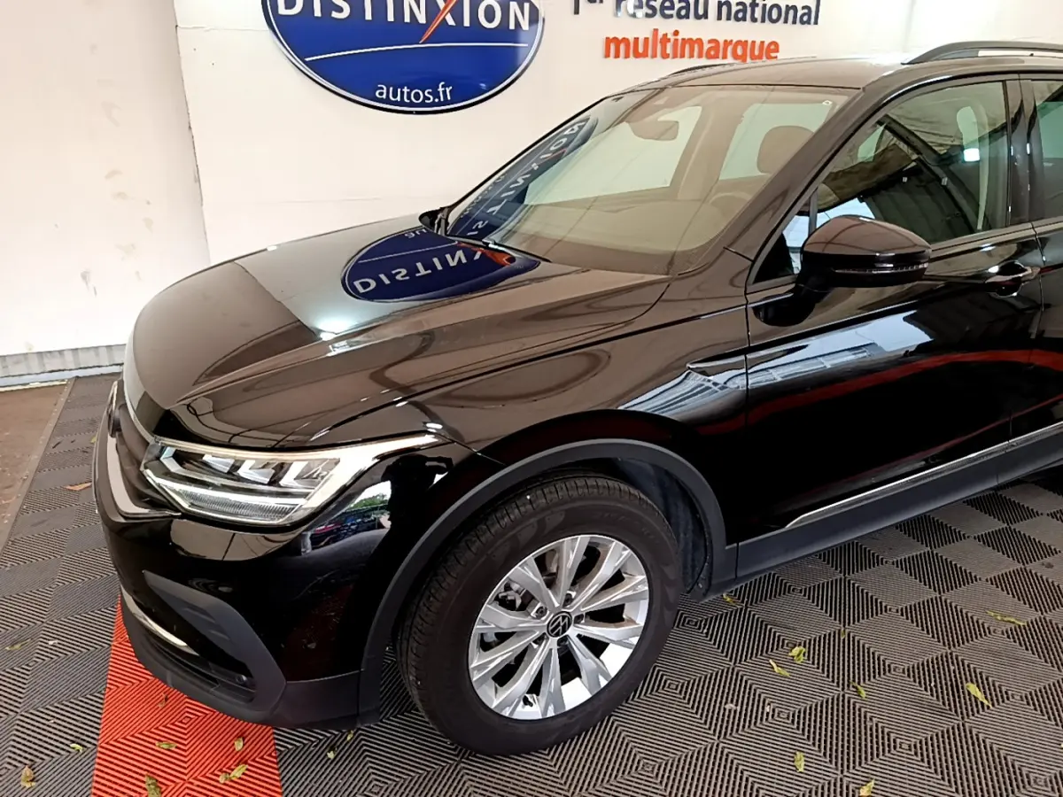 Vue 3/4 avant gauche d'un Volkswagen Tiguan noir brillant avec jantes alliage et phares LED allumés.
