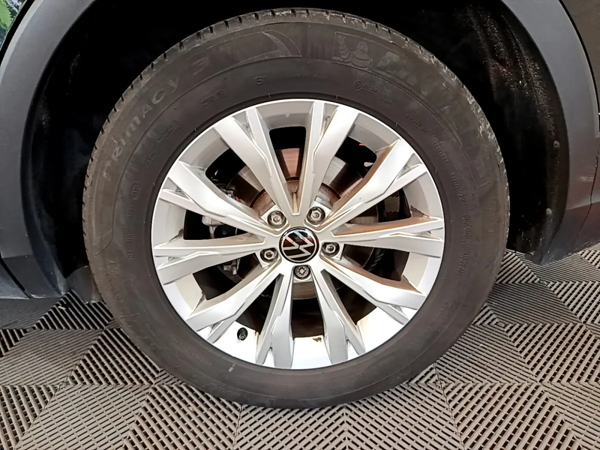 Gros plan sur la roue avant droite du Volkswagen Tiguan noir, mettant en valeur la jante alliage argentée et le logo VW.