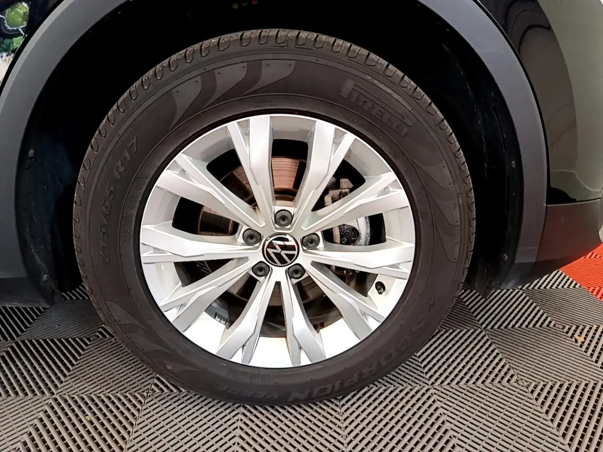 Gros plan sur la roue avant gauche du Volkswagen Tiguan noir, jante alliage argentée avec logo VW central.