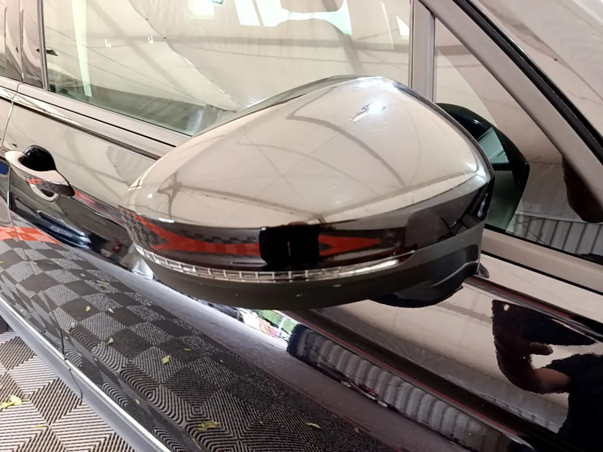 Gros plan sur le rétroviseur droit noir brillant du Volkswagen Tiguan 2021, reflet de l'environnement intérieur visible.