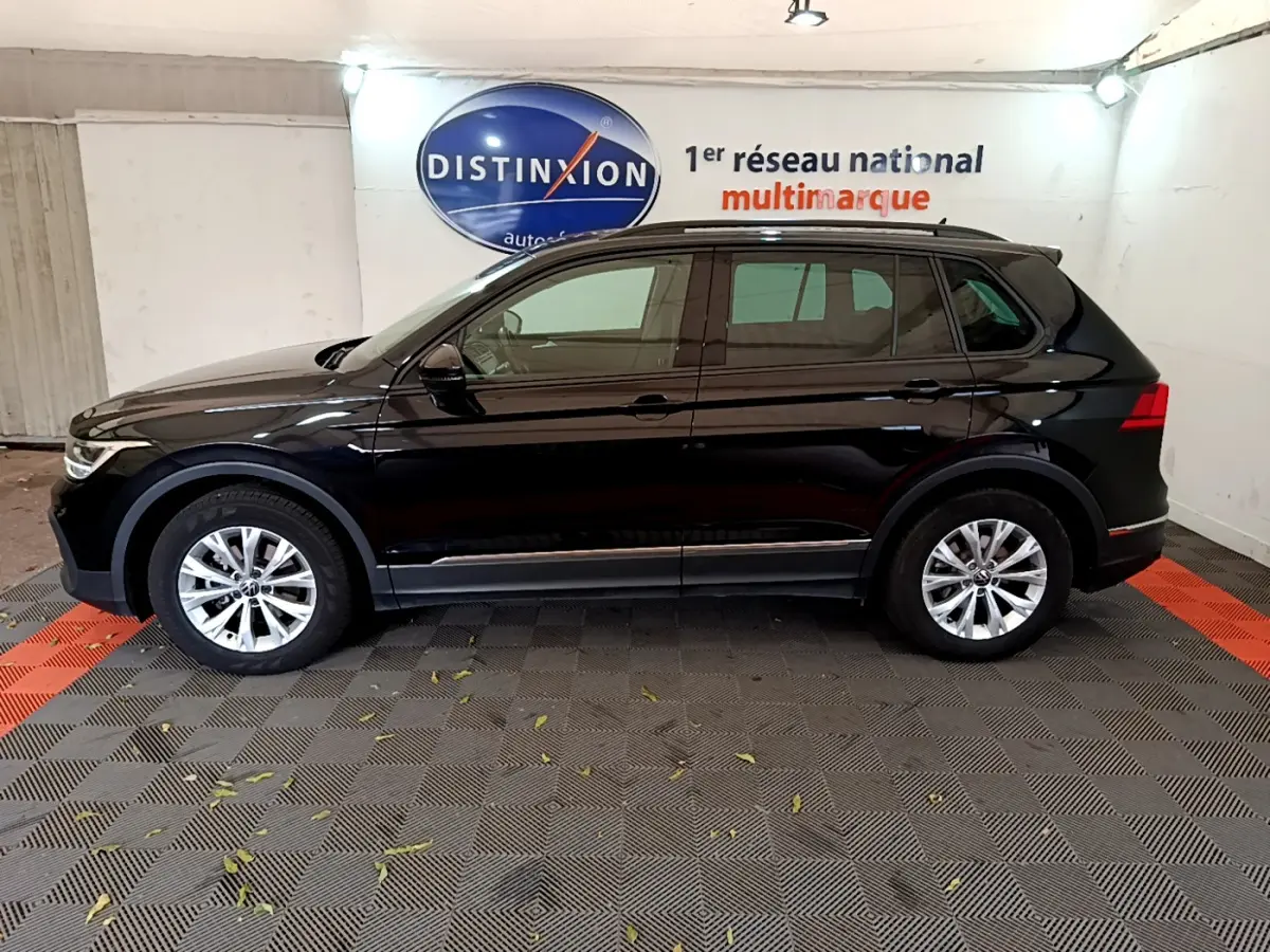 Profil côté gauche d'un Volkswagen Tiguan noir 2021 garé en intérieur avec jantes alliage et barres de toit noires.