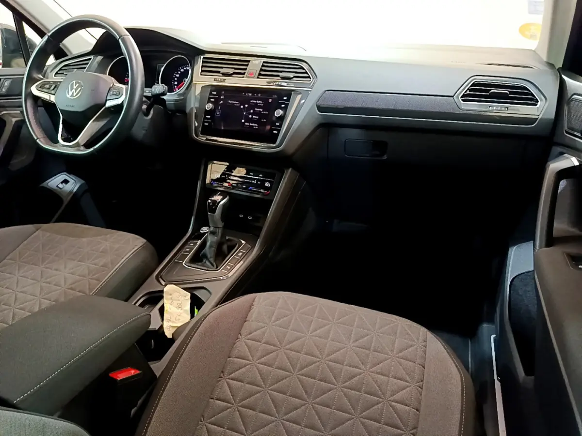Vue intérieure avant du Volkswagen Tiguan noir 2021, tableau de bord moderne avec écran tactile et volant cuir multifonctions.