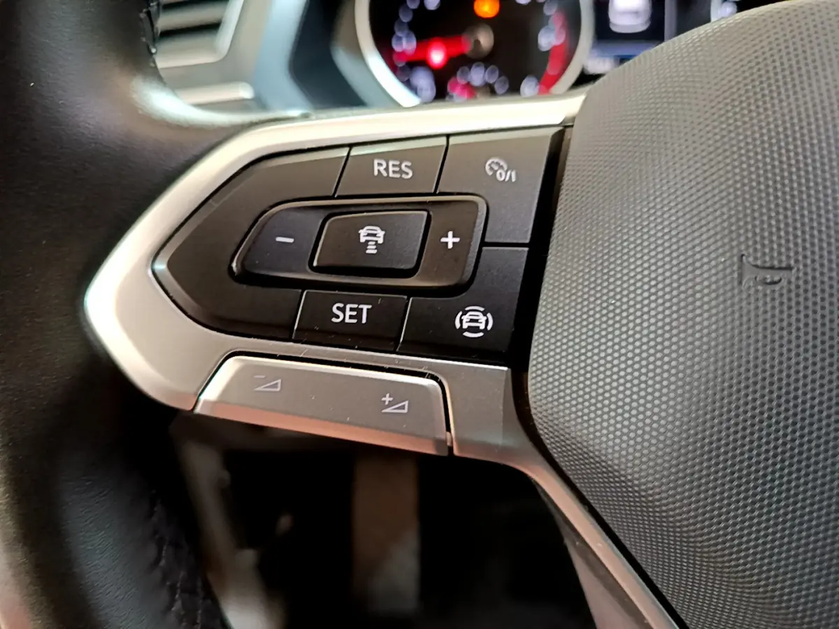 Gros plan sur les commandes du volant côté gauche du Volkswagen Tiguan noir, mettant en avant les boutons de régulateur de vitesse.
