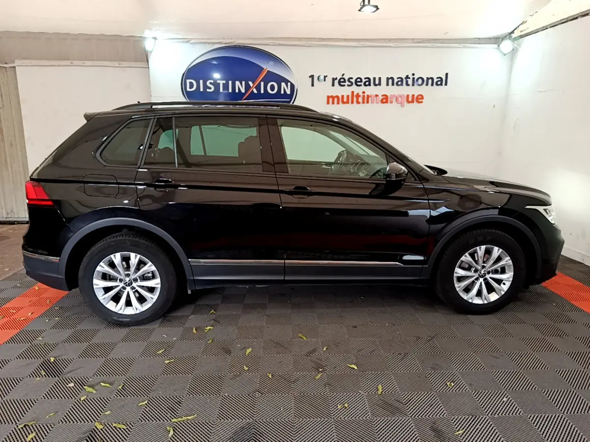 Profil côté gauche d'un Volkswagen Tiguan noir 2021 garé en intérieur avec jantes alliage et barres de toit noires.