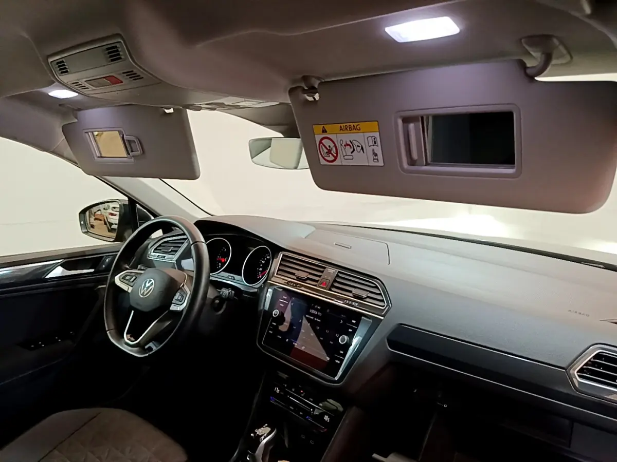 Vue intérieure côté conducteur du Volkswagen Tiguan 2021 avec tableau de bord noir et écran tactile central lumineux.