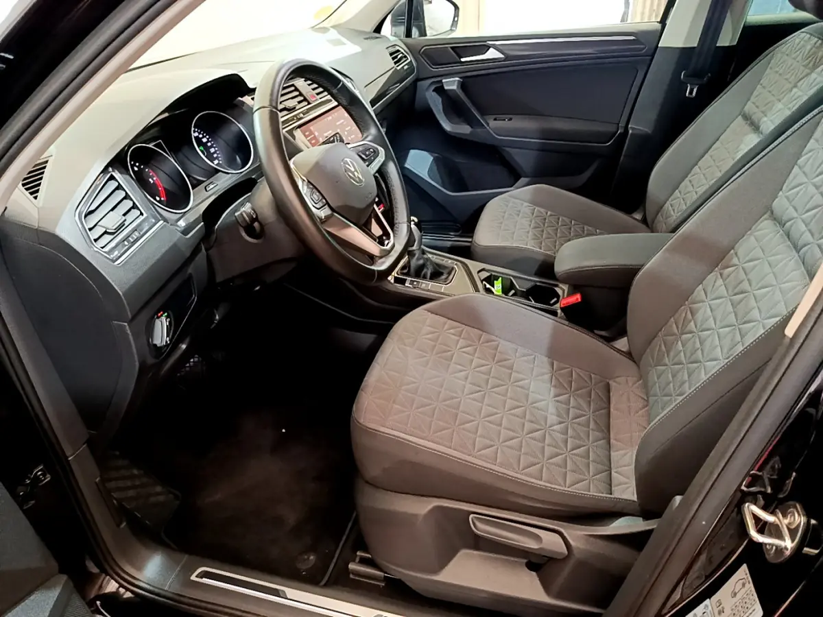 Vue intérieure côté conducteur du Volkswagen Tiguan noir 2021, sièges tissu gris à motifs géométriques et tableau de bord moderne.