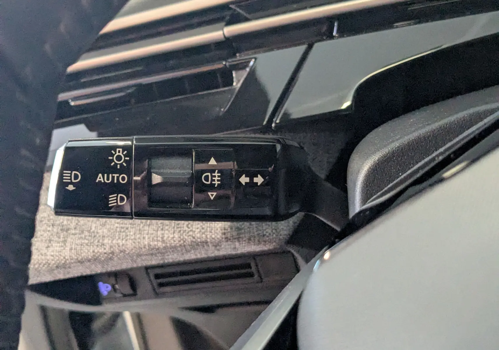 Gros plan sur la commande des feux à gauche du volant dans l’habitacle gris clair du Peugeot 3008 Hybrid blanc.