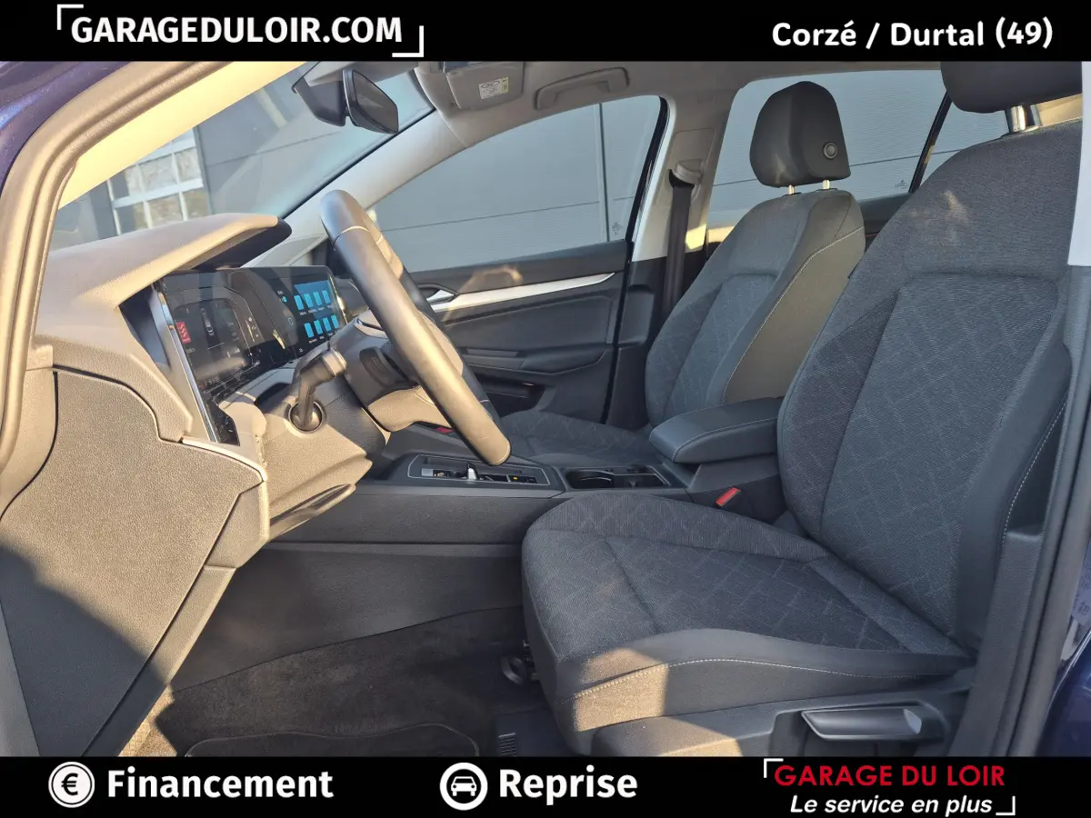 Vue intérieure côté conducteur de la Volkswagen Golf 2023 bleu, avec sièges tissu gris et tableau de bord digital.