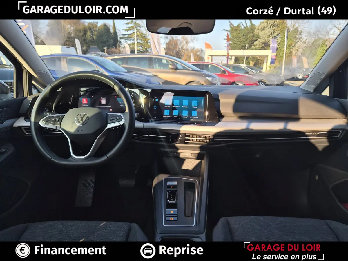 Vue intérieure avant de la Volkswagen Golf 2023, tableau de bord noir avec écran tactile central et volant cuir multifonctions.