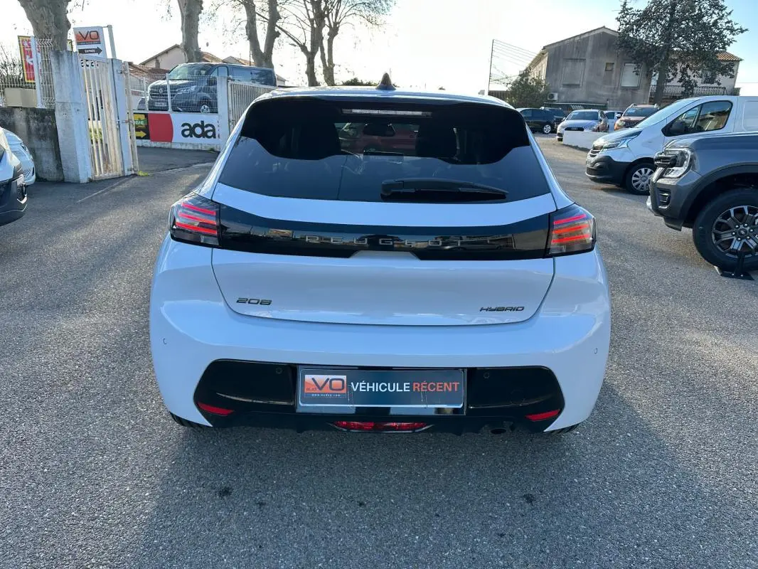 Vue arrière d'une Peugeot 208 Hybrid blanche, avec feux arrière LED et bande noire distinctive sur le hayon.