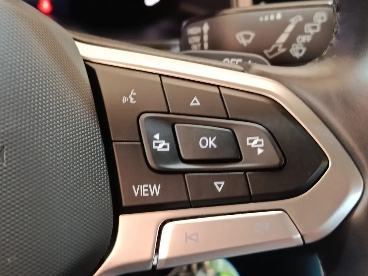 Gros plan sur les commandes multifonctions à gauche du volant du Volkswagen Taigo gris foncé, avec boutons noirs et cadre argenté.