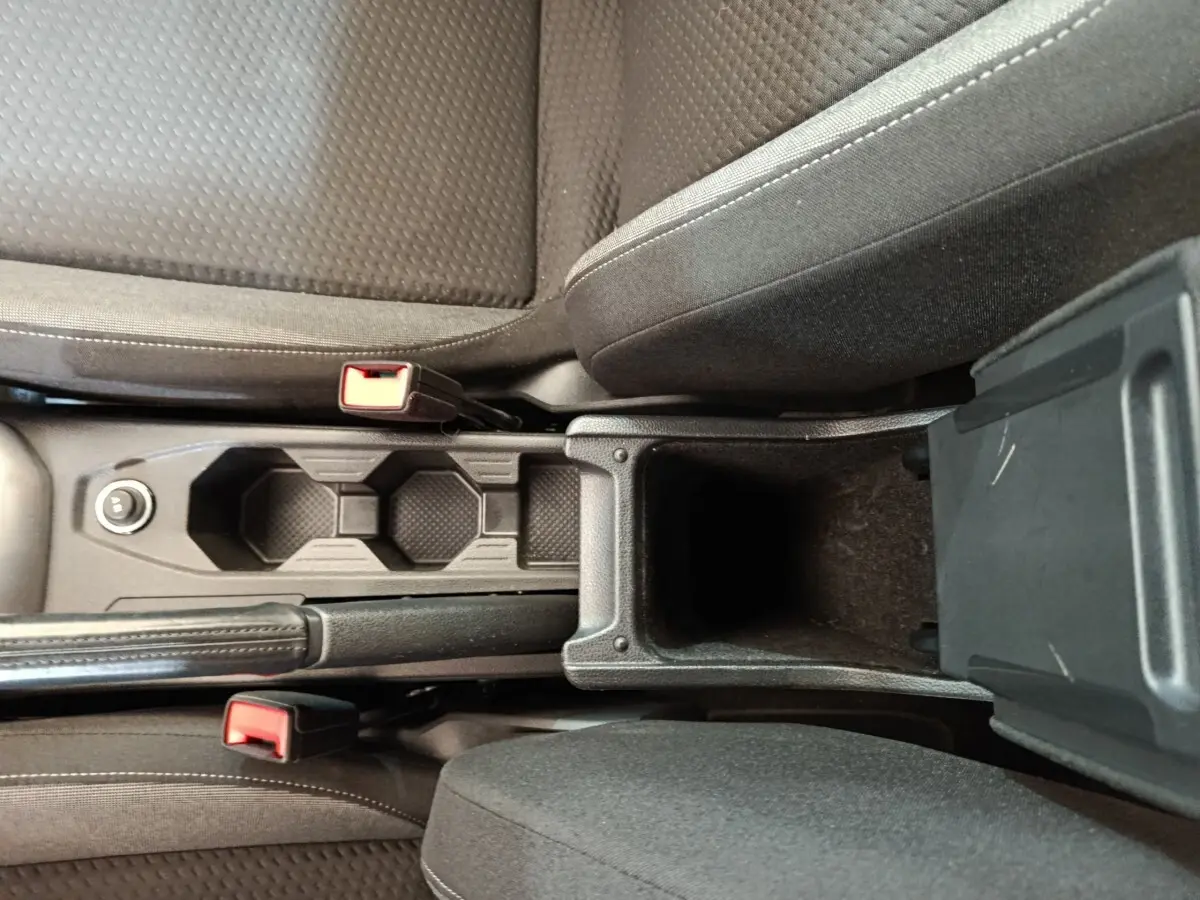 Vue plongeante sur la console centrale noire du Volkswagen Taigo 2023 avec porte-gobelets et accoudoir ouvert.